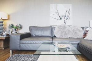 Große graue Ledercouch mit Glastisch, grauer Tapete und einem grau-weißem Bild einer Blume an der Wand