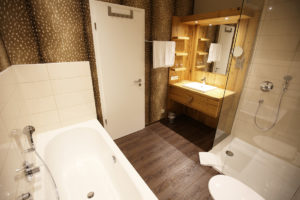 Badezimmer mit ebenerdiger Dusche, Badewanne, Toilette, weißem Waschbecken mit natürlichem Holzschrank und Spiegel