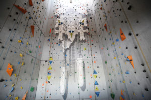 Frontalansicht grauer Kletterhalle Lüdenscheid der Sportalm Gipfelglück, riesige bayrische Kuckucksuhr als Motiv an der Wand