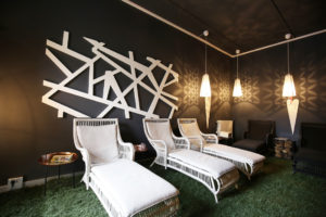 Weiße und schwarze Liegen inklusive Sitzkissen im beleuchteten Raum mit Kunstrasen als Bodenbelag