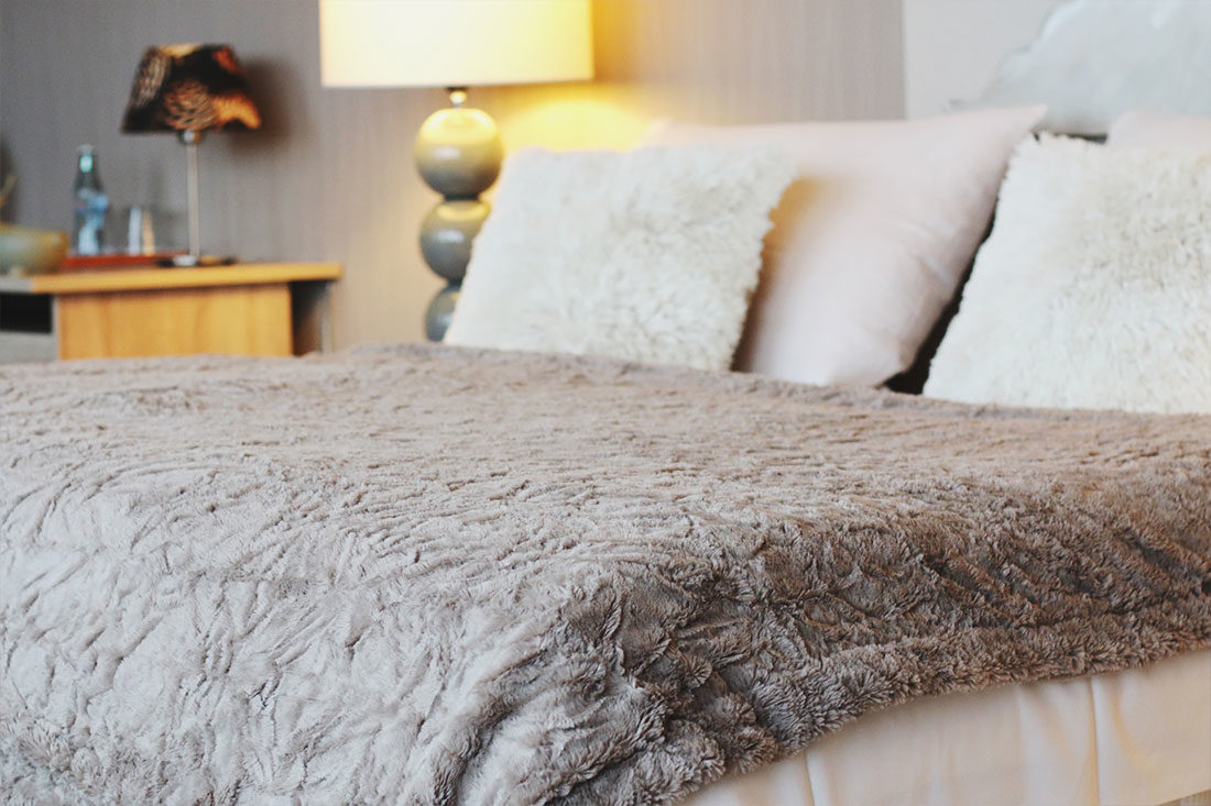 Doppelbett mit grauer Wolldecke und weißer Bettwäsche