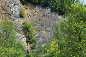 Bild auf dem ganz klein zwei Männer in der Natur zu sehen sind, die gerade an einer natürlichen Wand klettern