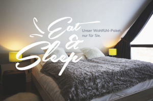 Schlafzimmer mit Doppelbett, weißer Bettwäsche, grauer Decke, weißer Text "Eat & Sleep. Unser Wohlfühl-Paket, nur für Sie."