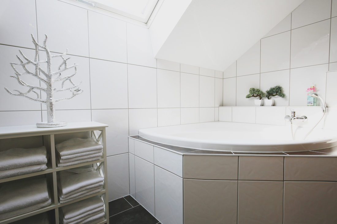 Große Badewanne in modernem Badezimmer, links ein Schränkchen mit Handtüchern