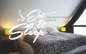 Schlafzimmer mit Doppelbett, weißer Bettwäsche, grauer Decke, weißer Text "Eat & Sleep. Unser Wohlfühl-Paket, nur für Sie."