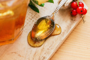 Teelöffel mit auslaufendem Honig auf Holzbrettchen