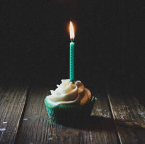 Kleiner Muffin mit Sahne und einer grünen Kerze die brennt