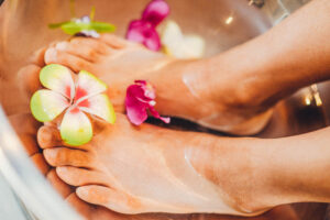 Zwei Füße im Wasser mit gelb-grüner Blume und rosa Blütenblättern
