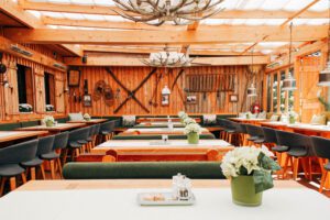 Großer bayrischer Raum mit Holztischen, grauen Stühlen und Holzbänken, durch die Decke scheint natürliches Licht